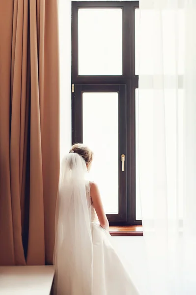 Braut im Brautkleid steht am Fenster im Zimmer und schaut hinaus — Stockfoto