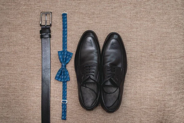 Blue bow tie, leather black shoes and belt. Grooms wedding morning. Close up of modern man accessories