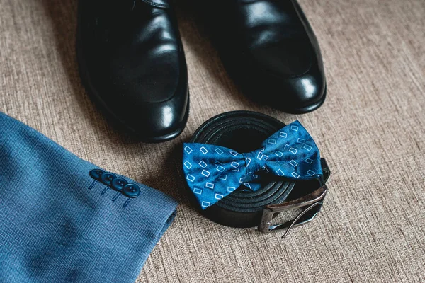 Suit, blue bow tie, leather black shoes and belt. Grooms wedding morning. Close up of modern man accessories