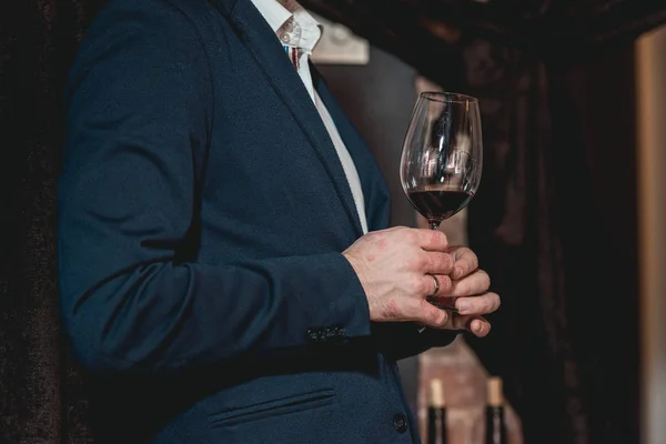 Hombre en un traje azul con una enfermedad de la piel sostiene un vaso de vino tinto. la gente considera el color del vino y probar cómo huele en diferentes vasos — Foto de Stock