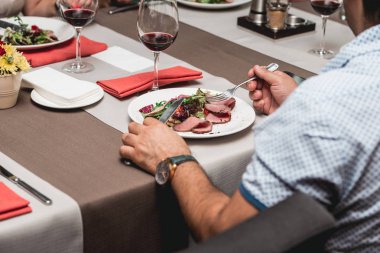 Adam masada bir restoranda taze et ve domates salatası yiyor