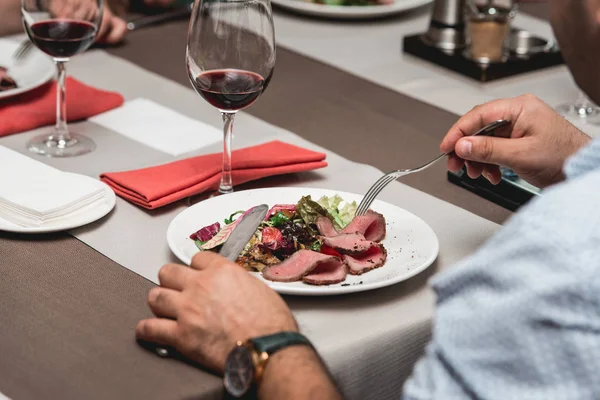 Человек за столом ест свежий салат с мясом и помидорами в ресторане — стоковое фото