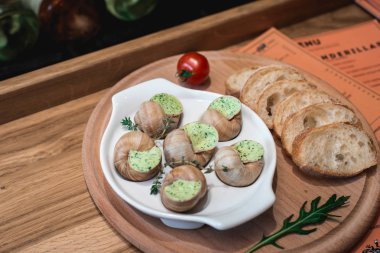 Salyangoz geleneksel seramik içinde otlar tereyağlı ekmek bir ahşap tahta üzerinde pan. Şarap