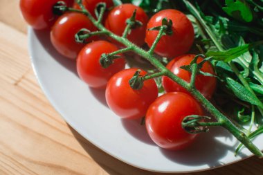 Bütün kırmızı domates kiraz ve taze yakut yaprakları kompozisyon ahşap masa üzerinde beyaz bir plaka üzerinde