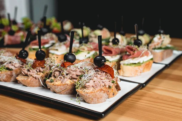 Sabrosos pinchos con atún, chorizos, salmón, huevo, tomates secos, aguacate, salmón, tocino, jamón, queso Brie, aceitunas y salsa de pesto, merienda tradicional española — Foto de Stock