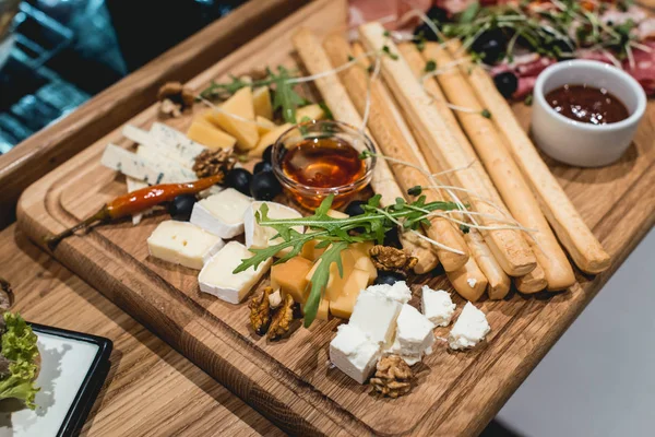 Prato de queijo: Emmental, queijo Camembert, queijo azul, paus de pão, nozes, azeitonas em mesa de madeira — Fotografia de Stock