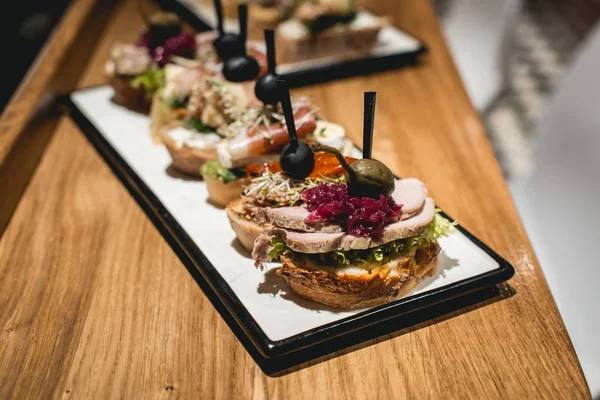 Pinchos saborosos com atum, chouriços, salmão, ovo, tomate seco, abacate, salmão, bacon, Hamon, queijo Brie, azeitonas e molho Pesto, lanche espanhol tradicional — Fotografia de Stock