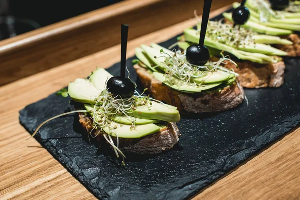 Saborosos pinchos com molho de pesto de abacate, oliva e manjericão, lanche tradicional espanhol, servido em uma prancha de pedra preta — Fotografia de Stock