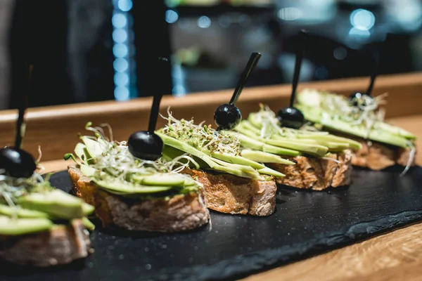 Saborosos pinchos com molho de pesto de abacate, oliva e manjericão, lanche tradicional espanhol, servido em uma prancha de pedra preta — Fotografia de Stock