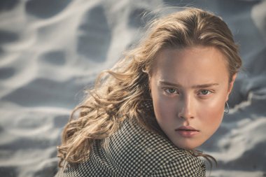 Sarışın kız kumsalda oturuyor. Güzel kıvırcık bir kadının açık hava portresi. güzellik rötuşı