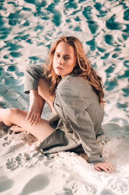 Sarışın kız kumsalda oturuyor. Güzel kıvırcık bir kadının açık hava portresi. güzellik rötuşı