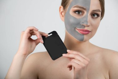 Kadın spa maskesi yarım yüz güzellik konsepti sağlıklı portre. Ellerinde Küçük Siyah Ürün Paketi