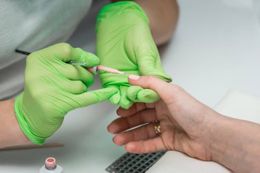 Yeşil eldivenli profesyonel manikür ustası kuaförde manikür yapıyor. SPA salonunda çivi tedavisi görüyor. Ayak hastalıkları kliniği.