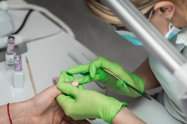 Yeşil eldivenli profesyonel manikür ustası kuaförde manikür yapıyor. SPA salonunda çivi tedavisi görüyor. Ayak hastalıkları kliniği.