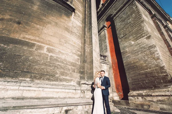 A noiva em um vestido de noiva branco e noivo em um terno no fundo de um edifício de tijolo — Fotografia de Stock