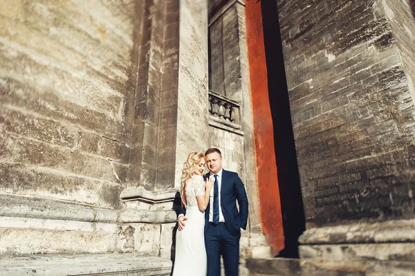 A noiva em um vestido de noiva branco e noivo em um terno no fundo de um edifício de tijolo — Fotografia de Stock