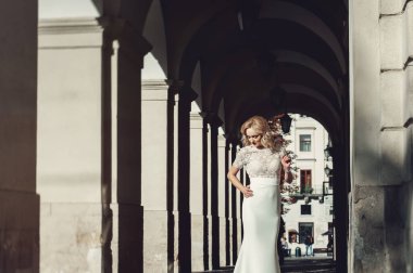 Güzel Mutlu Kıvırcık Saçlı Gelin 'in Portresi. Moda elbisesi ve Kırmızı Dudaklı Makyaj. Gelin, eski bir evin kemerinde duruyor.