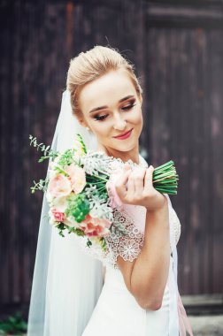 Güzel genç gelin elinde pastel bej renkte gül buketini Fransız manikürlü tutuyor. Yakın görünüm