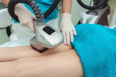 Beyaz eldivenli profesyonel bir dermatoloğun mavi havluyla bir kadının karnına radyofrekans kaldırma işlemi yaparken görüntüsü kesilmiş.