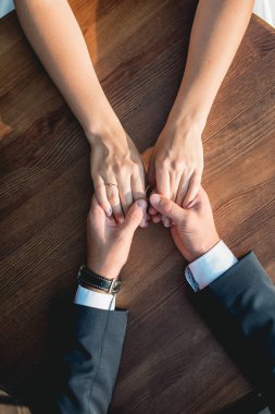 Sevgi dolu çift yuvarlak ahşap masada oturuyor, nazikçe el ele tutuşuyorlar. Yüksek açı görünümü.