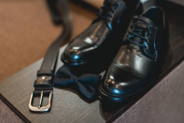 Modern erkek aksesuarlarını kapatın. Siyah papyon, deri ayakkabılar ve tahta bir masada kemer.