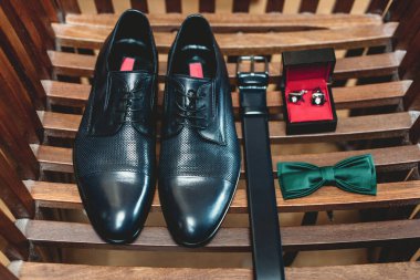 Sarı ahşap kalaslarda izole edilmiş zarif siyah erkek aksesuarları. Yüksek açılı kemer, ayakkabı, kol düğmesi ve yeşil papyon. Düğün konsepti hazırlığı.