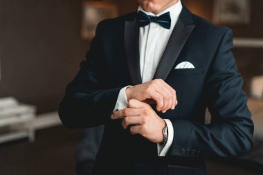 Siyah takım elbiseli bir adam gömleğine siyah kol düğmesi takıyor. Beyaz gömlek ve kol düğmesi takan bir adamın elini kapat..