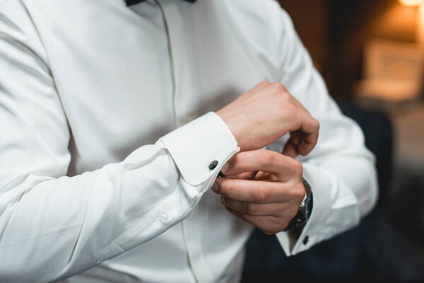 A man fastens black cufflink on the shirt. Close up of a man hand wearing a white shirt and cufflinks.