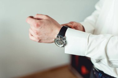 İş adamı kol saatini kontrol ediyor, saati eline alıyor, damat düğün töreninden önce hazırlanıyor.