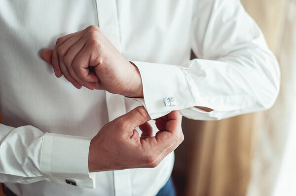 A man fastens cufflink on the white shirt. Close up of a man hand wearing a white shirt and cufflinks.
