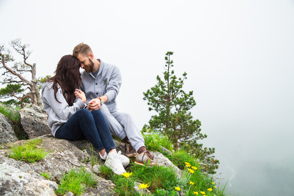 Happy young couple in love sitting on a mountain, hugging and lo
