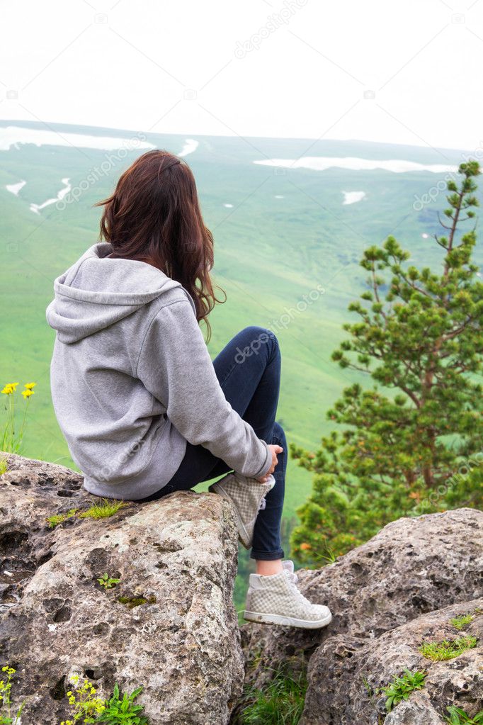Beautiful woman sitting on mountain top and contemplating landsc
