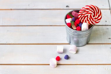 Küçük bir kova hafif ahşap arka plan üzerinde renkli şekerler wi