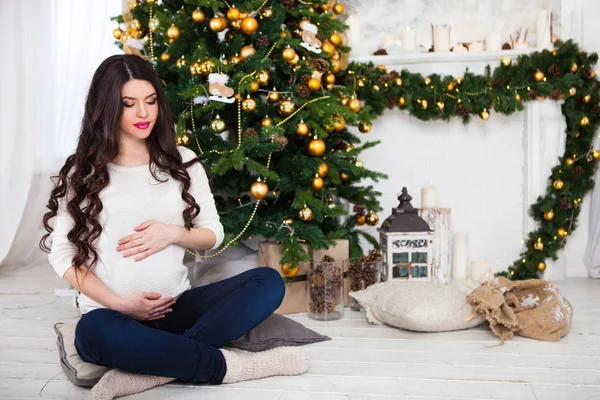 Mutlu hamile kadın Noel ağacının yanında oturuyor. — Stok fotoğraf