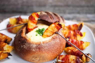 Tasty hot cheese fondue served in a bread roll with potatoes and clipart