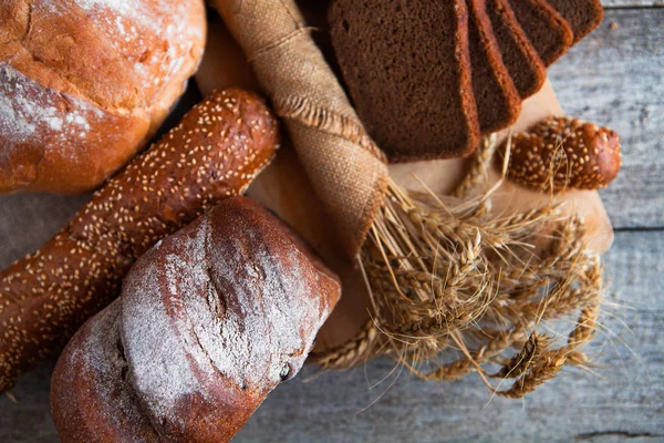 Pão fresco e trigo na velha mesa de madeira — Fotografia de Stock