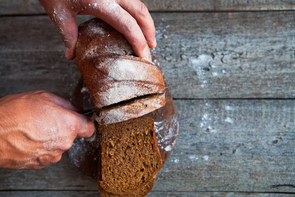 Mãos masculinas cortando pão caseiro fresco na mesa rústica — Fotografia de Stock
