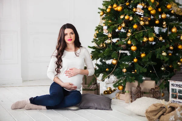 Mutlu hamile kadın Noel ağacının yanında oturuyor. — Stok fotoğraf