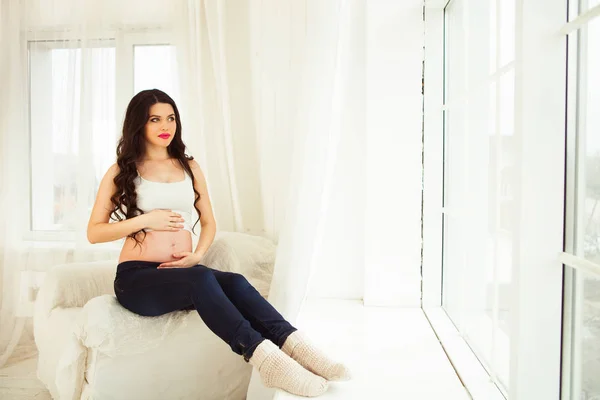 Joven mujer embarazada feliz sentada en la ventana de su casa — Foto de Stock