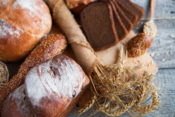 Pão fresco e trigo na velha mesa de madeira — Fotografia de Stock