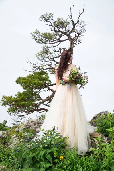 Schöne Braut mit Brautstrauß posiert in der Nähe von Felsen gegen b — Stockfoto