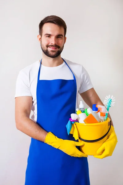 Homem segurando balde de plástico com garrafas e escovas, luvas e — Fotografia de Stock