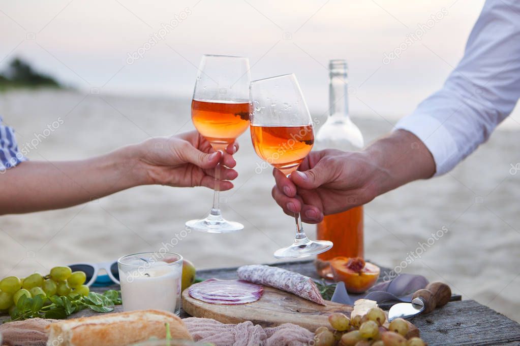 Man and woman clanging wine glasses with rose wine at sunset bea