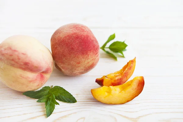 Свежие персики с мятой на деревянном белом фоне . — стоковое фото