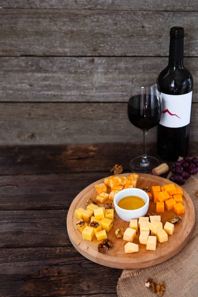 Uva, queijo, figos e mel com uma garrafa e um copo de vinho tinto — Fotografia de Stock