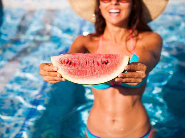 A girl holds half a red watermelon  over a blue pool, relaxing o — Stock Photo, Image