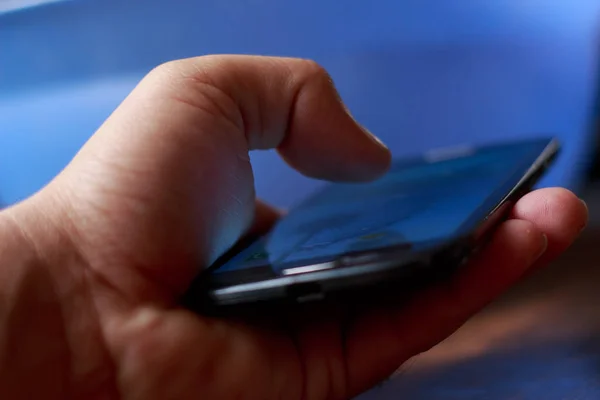Genç erkek el smartphone kullanarak closeup. Mavi arka plan bulanık — Stok fotoğraf