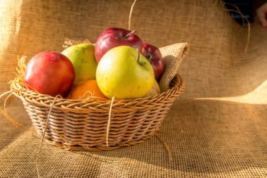 Sabah güneş çuval bezi zemin üzerine bir sepet içinde kırmızı ve yeşil elma.