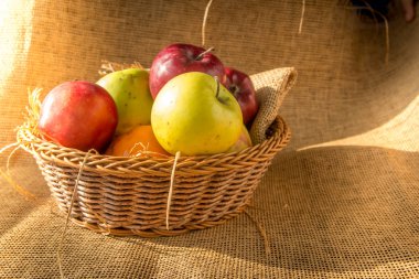 Sabah güneş çuval bezi zemin üzerine bir sepet içinde kırmızı ve yeşil elma.