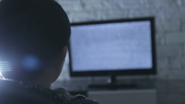 Pequeño niño viendo lcd TV en una habitación oscura con paredes de ladrillo estilo loft, vista trasera . — Vídeos de Stock